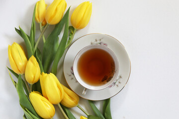A cup of tea and bunch of yellow tulips on white background. Concept of holiday, birthday, Easter, March 8. 