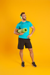 Fototapeta na wymiar Handsome man with yoga mat and headphones on yellow background