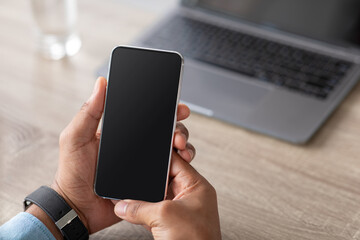 Unrecognizable millennial african american businessman holding smartphone with blank screen on workplace