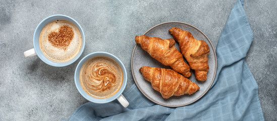 Fresh croissants and hot cups of coffee with hearts on rustic gray background. Top view, flat lay. Wide composition.