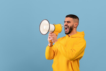 Emotional middle eastern man shouting with megaphone, making announcement or sharing news, blue background