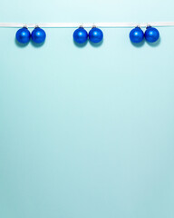 Dark blue christmas balls on white ribbon at the top side on blue background. Christmas winter holiday concept flat lay top view with copy space.