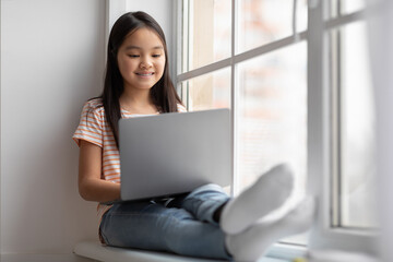 Beautiful chinese child using laptop, chilling at home