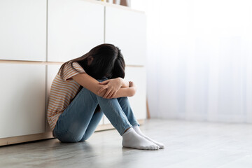 Upset long-haired brunette girl sitting on floor and crying