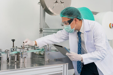 Engineer man wearing hygienic mask to protect coronavirus holding computer tablet checking and inspection machine in production line at factory industry.