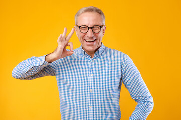 Happy mature man gesturing okay and smiling at studio