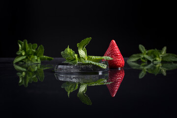 Una fresa con hojas de menta. Reflejo de espejo sobre fondo negro