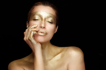 Gold skin woman. High fashion model girl with holiday shiny metallic gold makeup. Gold based beauty