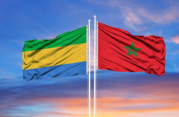 Morocco and Gabon two flags on flagpoles and blue cloudy sky