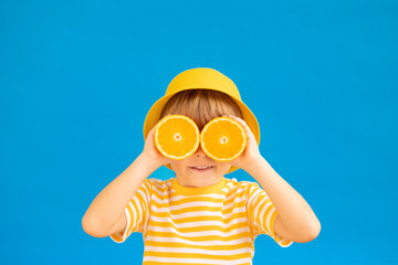 Happy child holding slices of orange fruit like sunglasses