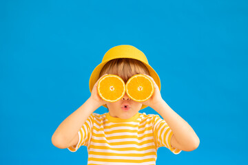 Surprized child holding slices of orange fruit like sunglasses - 478354984