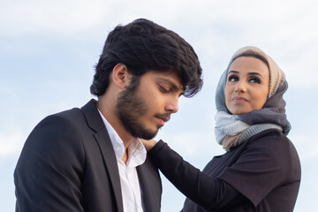 Loving Arabic couple spending time together. Woman with covered head and bright make-up and man in suit walking on bridge. Love, affection concept