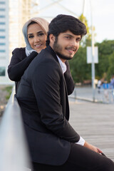 Affectionate Arabic couple spending time together. Woman with covered head and bright make-up and man in suit sitting on bench. Love, affection concept