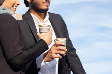 Close-up of loving Arabic couple during walk. Woman with covered head and man in suit standing together, holding disposable cups of coffee. Love, affection concept