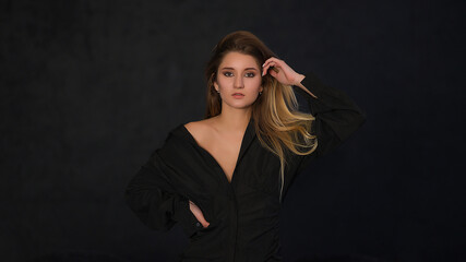 Portrait of a blonde girl on a black background. Beautiful curly hair. The girl looks at the camera. Girl in a black dress.