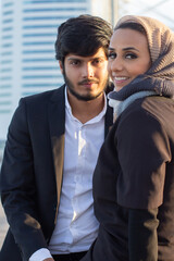 Beautiful Arabic couple spending time together. Woman with covered head and bright make-up and man in suit sitting looking at camera. Love, affection concept