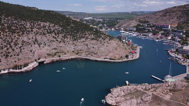 Aerial view of the landscape with a pier for yachts and boats on the Mediterranean strait between the mountains. Sailing yachts and boats on sea water. Stock footage. Amazing aerial cityscape view