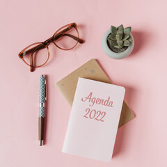 Agenda 2022 sur fond rose avec lunettes, stylo plume et succulent dans un style féminin