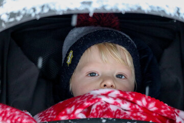 baby child peeks out of the stroller in winter