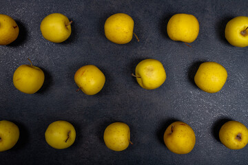 Apples are golden on a black background. Bright yellow apples are scattered on the black stone table