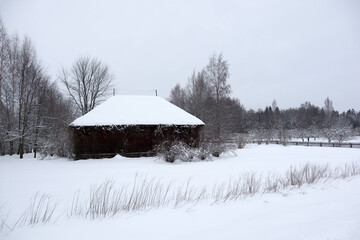 snow covered old brown wooden house in the winter field