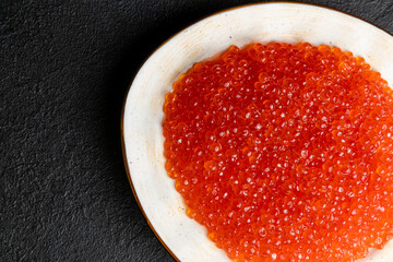 red caviar on a white plate, dark background, delicacy red caviar