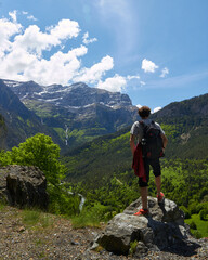 vertical image of a mountaineer enjoying the landscape in front of him, in which he can see sky, mountains, waterfalls and rivers,