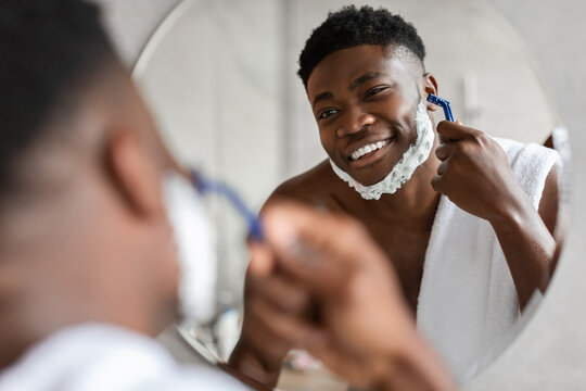 Black Man Removing Hair Shaving Face Using Razor In Bathroom