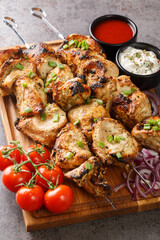 Homemade chicken kebab on skewers with vegetables and two sauces close-up in a wooden board on gray concrete background. Vertical