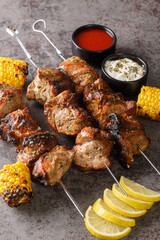 Juicy shish kebab on skewers with grilled corn and two sauces close-up on a gray concrete background. vertical