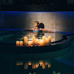 Beauty woman relaxing in the hot pool with candles in the evening