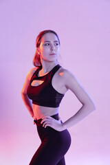 Young slender woman engaged in fitness on light background. Posing at cyclorama. Trendy multicolor neon lighting.