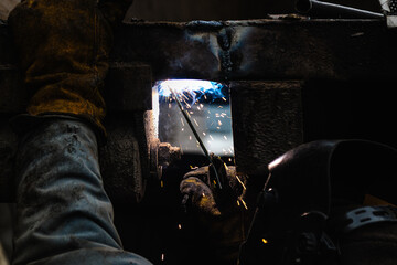 a welder in a protective mask welds iron structures in a factory