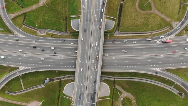 Automobiles and lorries drive along marked multilevel overpass highway with fork and grassy lanes on gloomy day aerial view