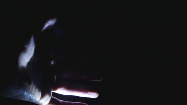 A man warms his hands after hypothermia while sitting by a warm hearth in the dark. Water vapor escapes from the skin. Extreme living conditions