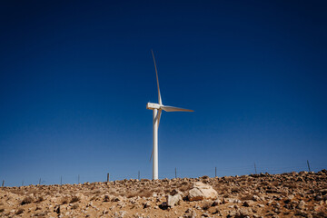 Fototapeta White mill on a clear day against the blue sky in the desert. Landscape with desert hills and white windmill obraz