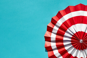 Red and white striped circular pleated paper origami fan on blue cyan bright background with space for text. Summer concept.