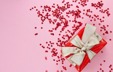 Preparing for different holidays. Red gift box with gold bow and red sequins on a pink background. Copy space.