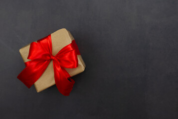 Gift box with red bow on a black background. Festive background. Copy space.