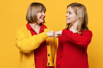 Happy woman 50s in red shirt have fun with teenager girl 12-13 years old Grandmother granddaughter do fist bump gesture look to each other isolated on plain yellow background Family lifestyle concept