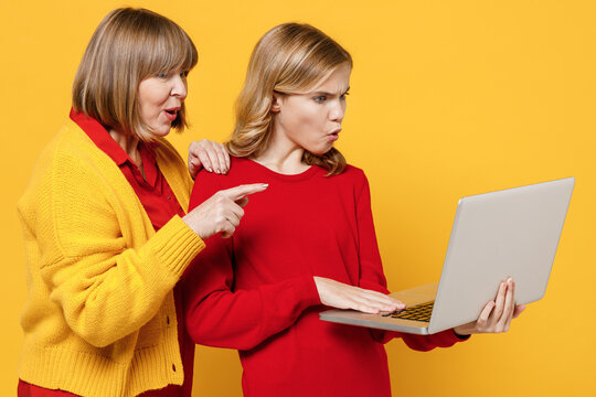 Scared Woman 50s In Red Shirt With Teenager Girl 12-13 Years Old. Grandmother Granddaughter Hold Use Work Point On Laptop Pc Computer Isolated On Plain Yellow Background. Family Lifestyle Concept.