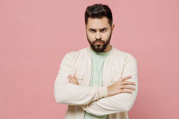 Young sad offended frowning caucasian man 20s wearing trendy jacket shirt hold hands crossed folded look camera isolated on plain pastel light pink background studio portrait People lifestyle concept