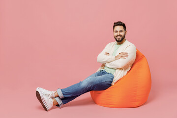 Full body young smiling cheerful friendly happy caucasian man 20s wearing trendy jacket shirt sit in bag chair isolated on plain pastel light pink background studio portrait. People lifestyle concept.