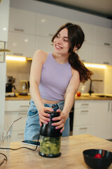 Sporty young woman is preparing healthy food on light kitchen.