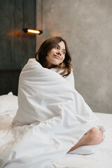 Beautiful young woman wrapped with soft blanket on bed after awakening.