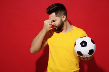 Tired sad young bearded man football fan in yellow t-shirt cheer up support favorite team hold...