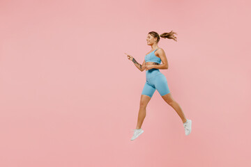 Fototapeta na wymiar Full length young athletic fitness trainer instructor woman wearing blue tracksuit spend time in home gym jump high point finger aside on area isolated on plain pink background. Workout sport concept