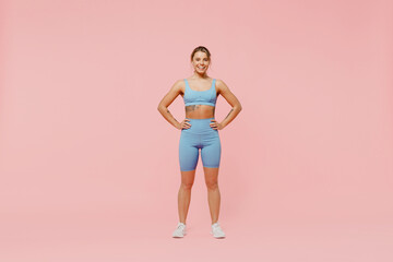 Full body young strong sporty athletic fitness trainer instructor woman wear blue tracksuit spend time in home gym hold hands on waist isolated on pastel plain pink background. Workout sport concept.