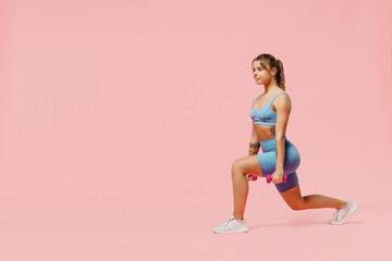 Obraz na płótnie Canvas Full size young sporty athletic fitness trainer instructor woman wear blue tracksuit spend time in home gym hold dumbbells do stretch squats isolated on plain pink background. Workout sport concept