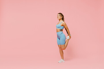 Full body young sporty athletic fitness trainer woman wear blue tracksuit spend time in home gym train do stretch legs exercise isolated on pastel plain light pink background. Workout sport concept. - obrazy, fototapety, plakaty